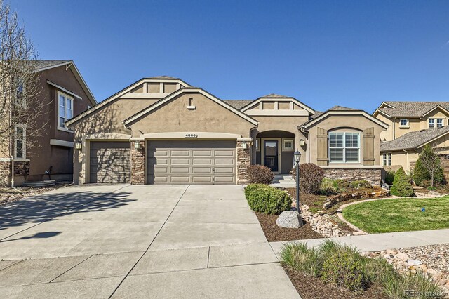 4866 Rainbow Gulch Trl, Colorado Springs, CO 80924 - view of front facade featuring stucco siding, stone siding, a garage, and driveway