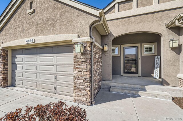 4866 Rainbow Gulch Trl, Colorado Springs, CO 80924 - view of exterior entry featuring stucco siding, stone siding, driveway, and a garage