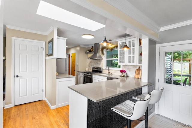 11224 W 28th Pl, Lakewood, CO 80215 - kitchen with stainless steel gas range oven, wall chimney range hood, a skylight, a breakfast bar area, and light wood-style floors