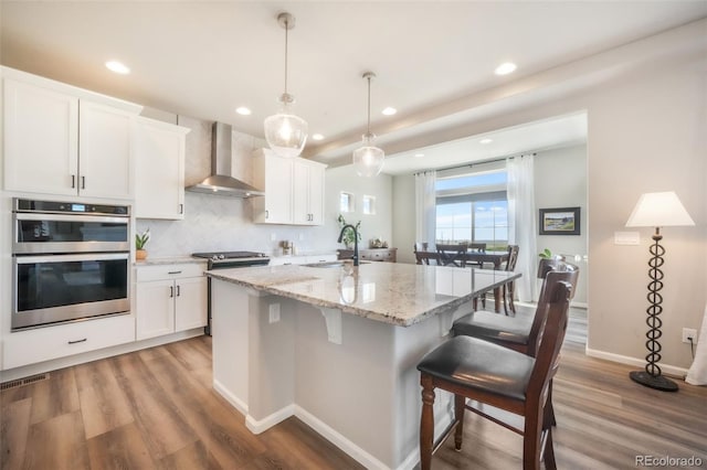 9521 Sideoats Ct, Colorado Springs, CO 80927 - kitchen featuring wall chimney range hood, stainless steel double oven, recessed lighting, a center island with sink, and a kitchen bar