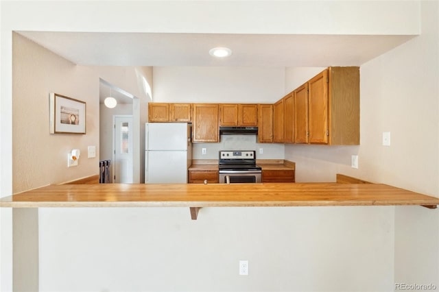 kitchen with brown cabinetry, stainless steel range with electric stovetop, a peninsula, under cabinet range hood, and freestanding refrigerator