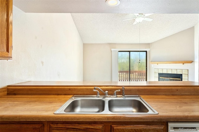 kitchen with a sink, a textured ceiling, brown cabinets, ceiling fan, and a tile fireplace