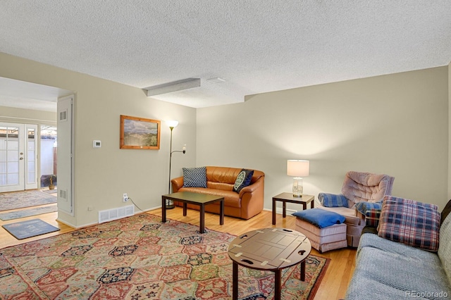 living room with french doors, a textured ceiling, and light wood-type flooring