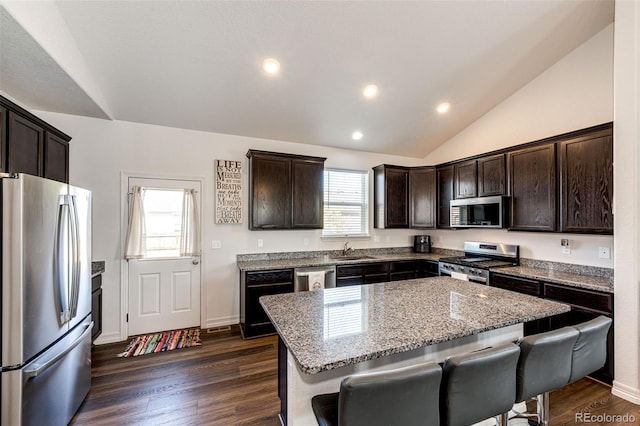 kitchen with a breakfast bar, a center island, vaulted ceiling, appliances with stainless steel finishes, and light stone countertops