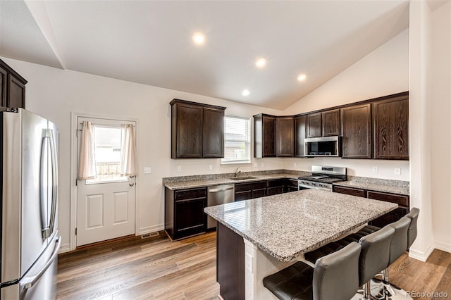 56459 E 23rd Pl, Strasburg, CO 80136 - kitchen with appliances with stainless steel finishes, dark brown cabinetry, light stone countertops, a center island, and light wood-style flooring