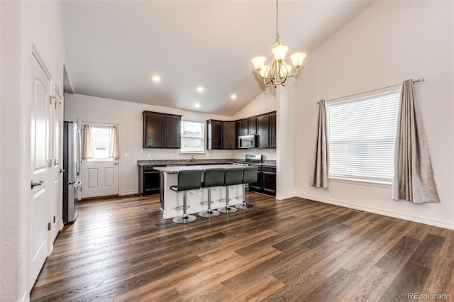 56459 E 23rd Pl, Strasburg, CO 80136 - kitchen with appliances with stainless steel finishes, a chandelier, vaulted ceiling, dark brown cabinets, and a kitchen island