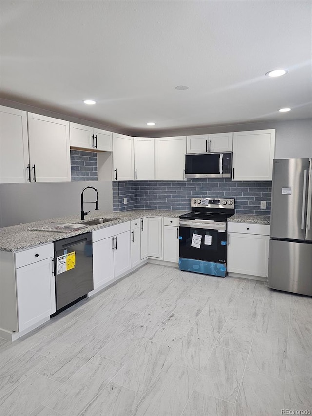 kitchen with sink, decorative backsplash, light stone countertops, appliances with stainless steel finishes, and white cabinetry