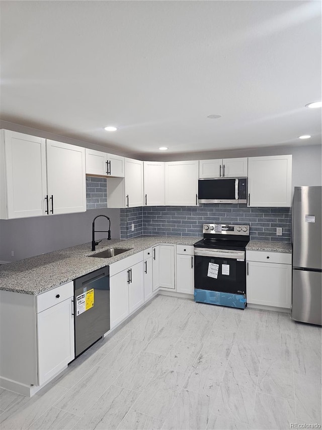 kitchen with sink, appliances with stainless steel finishes, tasteful backsplash, light stone counters, and white cabinetry