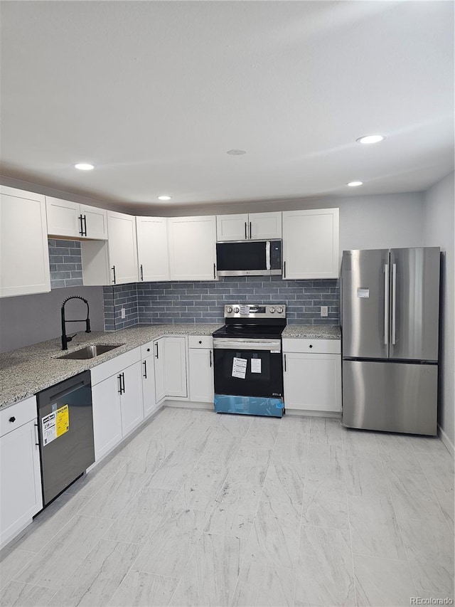 kitchen with decorative backsplash, appliances with stainless steel finishes, light stone counters, sink, and white cabinetry