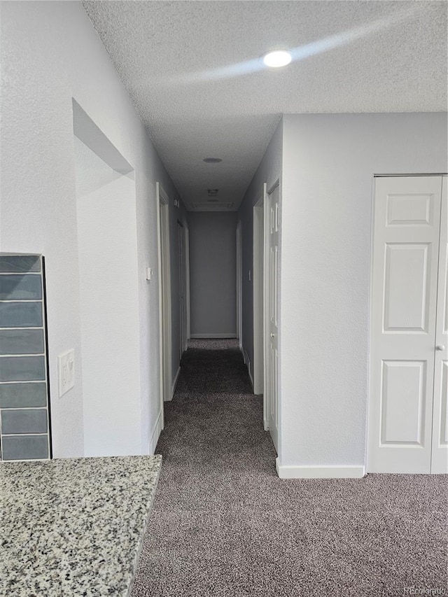 hallway with dark colored carpet and a textured ceiling