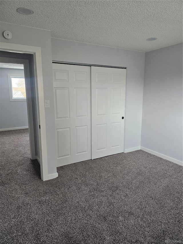 unfurnished bedroom with dark colored carpet, a textured ceiling, and a closet