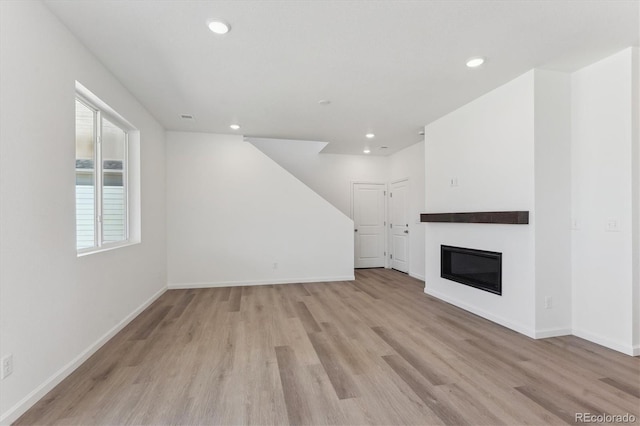 unfurnished living room featuring baseboards, light wood-style floors, a glass covered fireplace, and recessed lighting