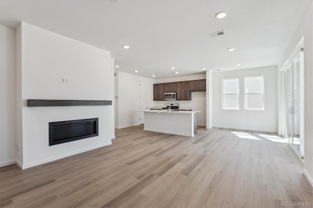 unfurnished living room with light wood finished floors, a glass covered fireplace, visible vents, and recessed lighting