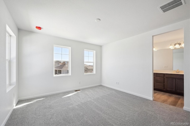 unfurnished bedroom featuring a sink, carpet, baseboards, and visible vents