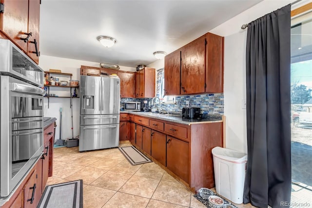 kitchen with brown cabinets, light tile patterned floors, stainless steel appliances, tasteful backsplash, and a sink