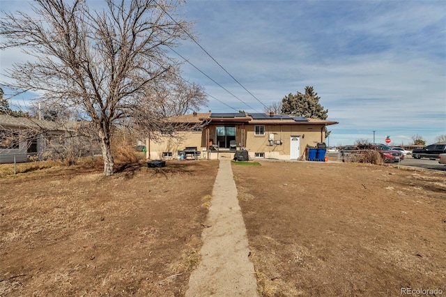 rear view of property featuring fence and solar panels