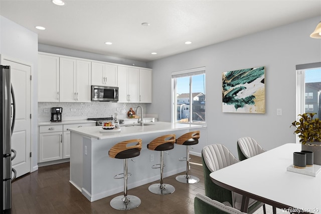 kitchen featuring stainless steel appliances, white cabinetry, backsplash, dark hardwood / wood-style flooring, and a kitchen island with sink