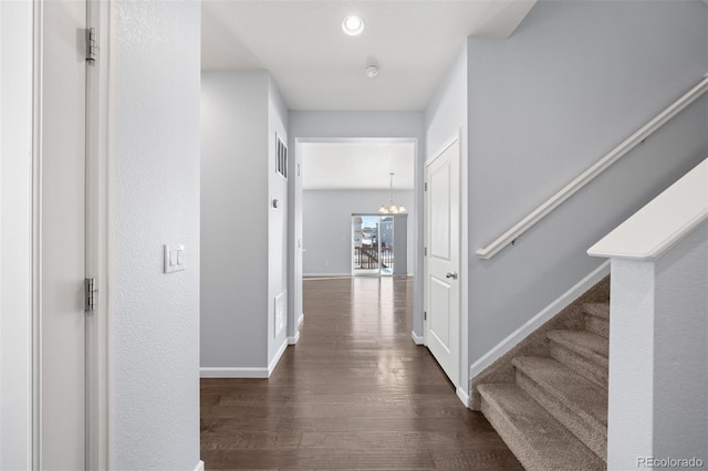 hall with dark wood-type flooring and a notable chandelier