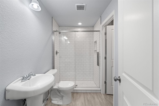 bathroom with toilet, hardwood / wood-style flooring, a shower with door, and sink