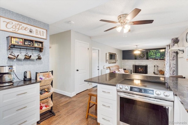 915 Mercury Cir, Littleton, CO 80124 - kitchen with electric range, white cabinetry, a ceiling fan, a fireplace, and wood finished floors