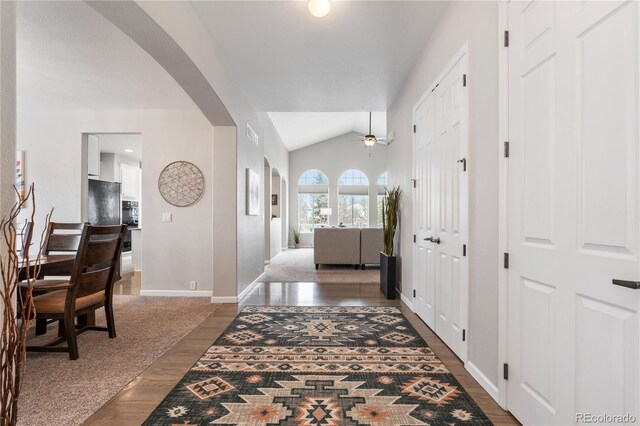 foyer entrance with ceiling fan, baseboards, vaulted ceiling, wood finished floors, and arched walkways