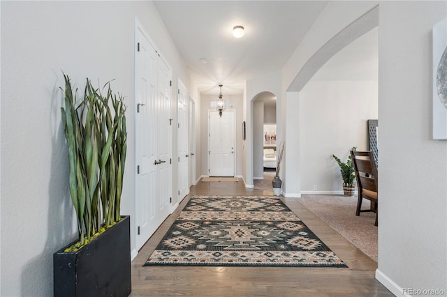 foyer featuring baseboards, arched walkways, and wood finished floors