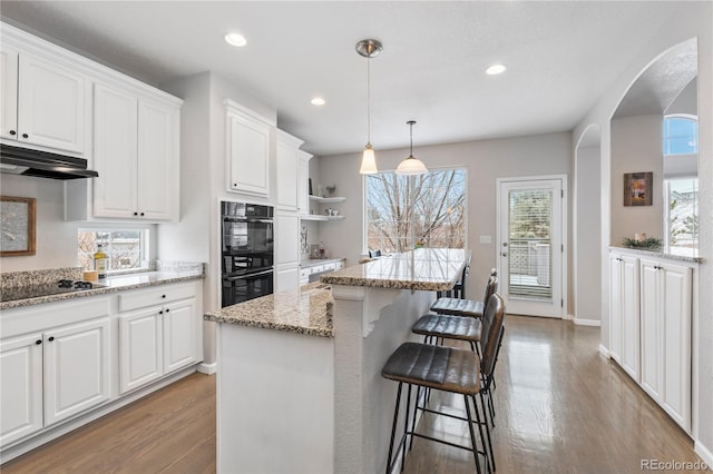 kitchen with a breakfast bar area, black appliances, white cabinets, under cabinet range hood, and light wood-type flooring