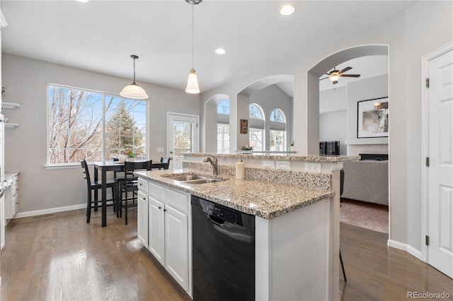 kitchen with a sink, light stone counters, black dishwasher, wood finished floors, and arched walkways