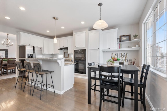 kitchen with under cabinet range hood, white cabinets, wood finished floors, stainless steel fridge, and dobule oven black