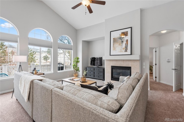 living area with baseboards, a tiled fireplace, light colored carpet, arched walkways, and high vaulted ceiling