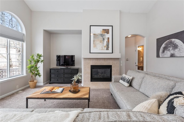 carpeted living room with a wealth of natural light, arched walkways, a tiled fireplace, and baseboards