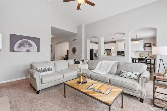 living area featuring visible vents, light carpet, arched walkways, baseboards, and ceiling fan