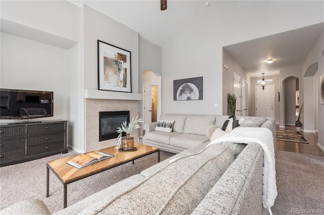 living room with high vaulted ceiling, a tiled fireplace, arched walkways, carpet flooring, and baseboards