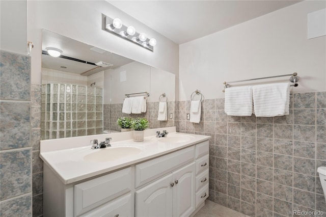 bathroom with double vanity, a walk in shower, tile walls, and a sink