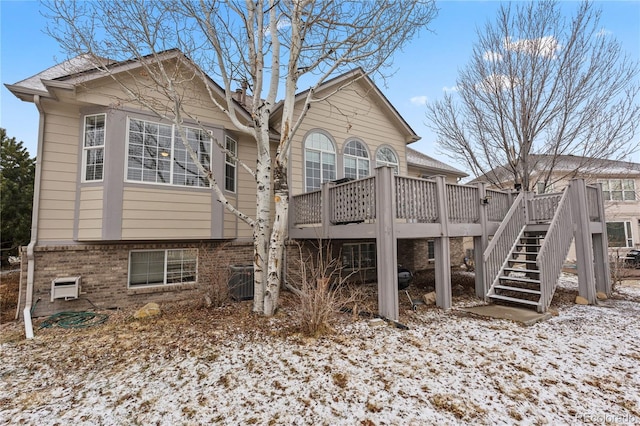 rear view of house featuring brick siding, a wooden deck, stairs, and central AC