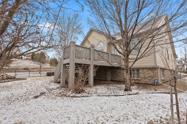 snow covered property with a deck, stairway, fence, and brick siding