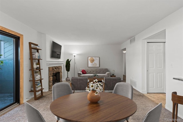 dining space featuring visible vents, light colored carpet, and a stone fireplace