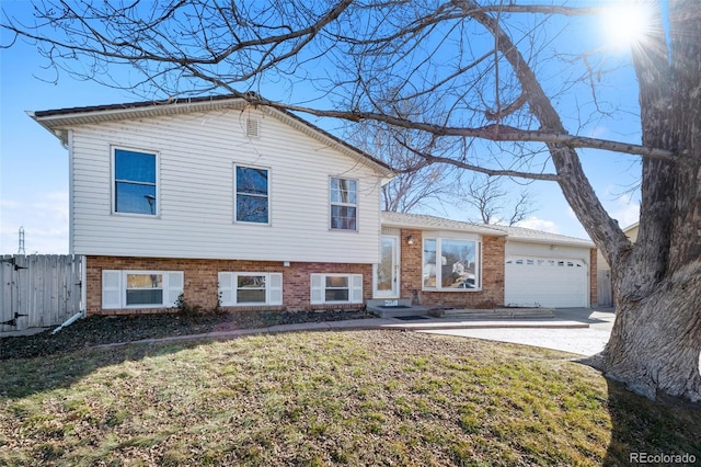 tri-level home featuring a garage, driveway, brick siding, and fence