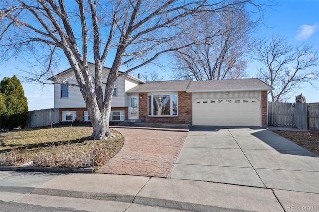 split level home with a garage, fence, concrete driveway, and brick siding