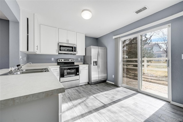 kitchen with stainless steel appliances, white cabinetry, sink, and light hardwood / wood-style flooring