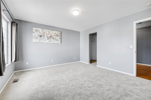 unfurnished bedroom featuring a walk in closet, light carpet, and a closet