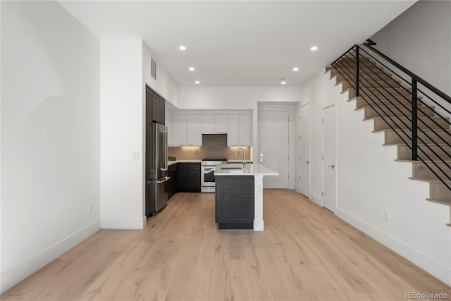 kitchen with sink, stainless steel appliances, light hardwood / wood-style floors, and an island with sink