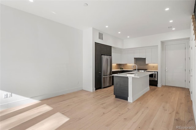 kitchen featuring white cabinetry, sink, high end refrigerator, light hardwood / wood-style flooring, and a kitchen island with sink