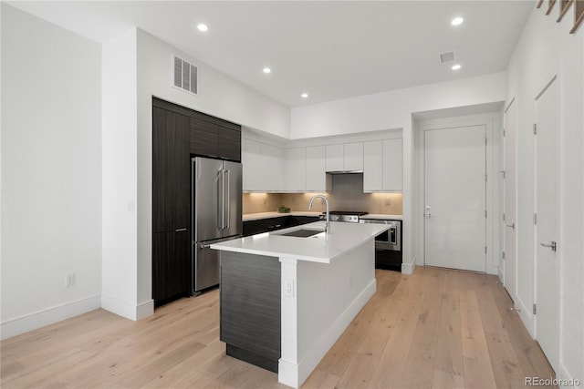 kitchen with high end fridge, an island with sink, light hardwood / wood-style floors, and sink