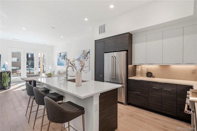 kitchen with high end refrigerator, visible vents, modern cabinets, a kitchen bar, and a sink