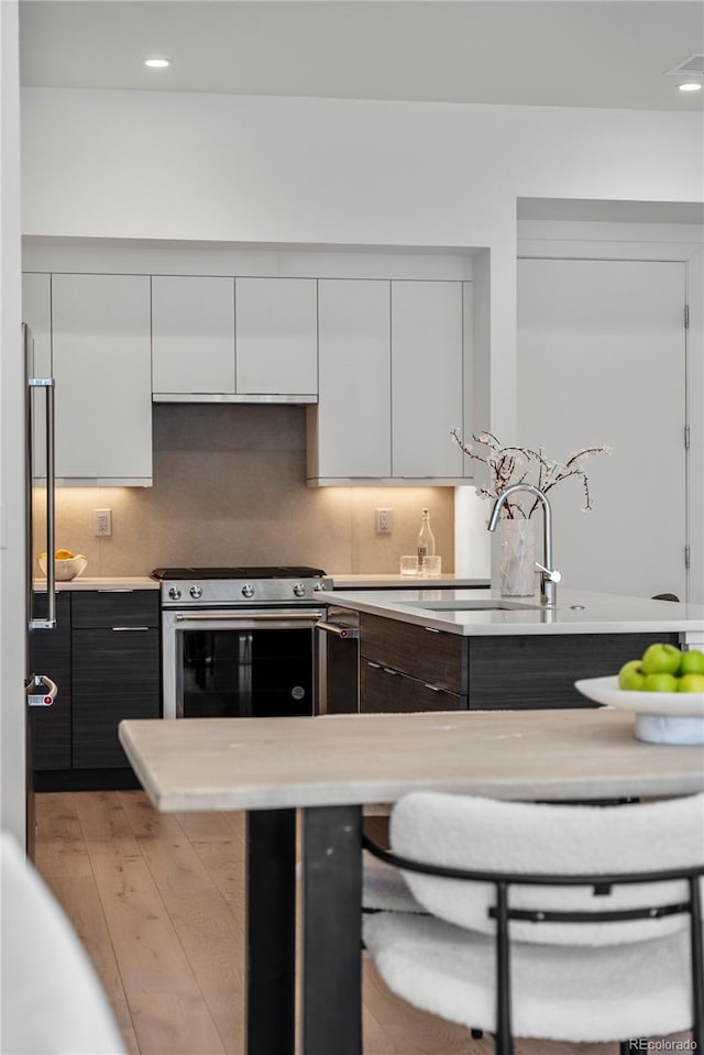 kitchen with light wood-style floors, light countertops, white cabinetry, and stainless steel gas range oven