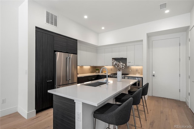 kitchen with visible vents, modern cabinets, high quality fridge, a breakfast bar area, and a sink