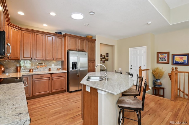 23285 Chapel Hill Ln, Parker, CO 80138 - kitchen featuring appliances with stainless steel finishes, a kitchen bar, light wood-style floors, brown cabinetry, and decorative backsplash