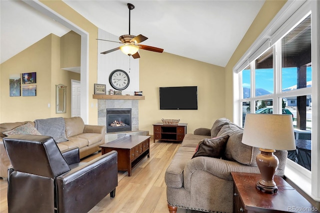 living area featuring a tiled fireplace, light wood finished floors, ceiling fan, and high vaulted ceiling