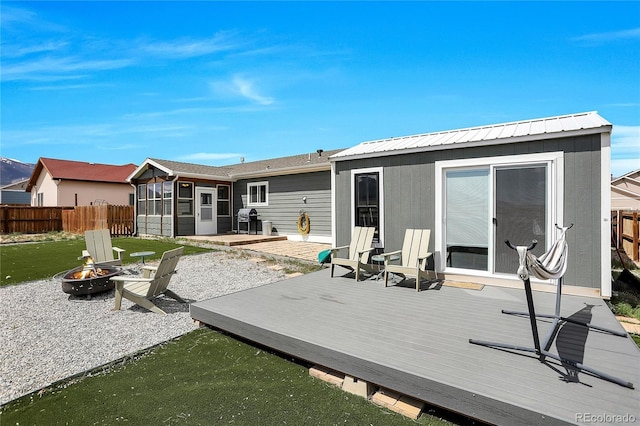 rear view of house with a fire pit, a wooden deck, fence, a sunroom, and metal roof